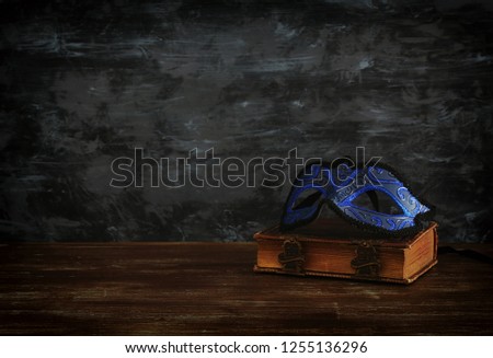 Image of elegant royal blue venetian mask over vintage old book in front dark wooden background