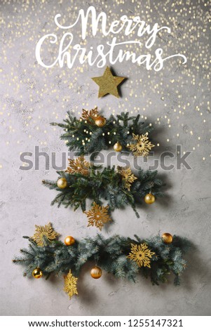 handmade Christmas tree and star hanging on grey wall with "merry christmas" lettering and glowing lights