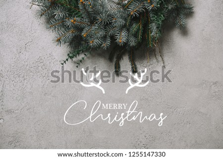 cropped image of fir wreath for Christmas decoration hanging on grey wall with "merry christmas" lettering with deer horns
