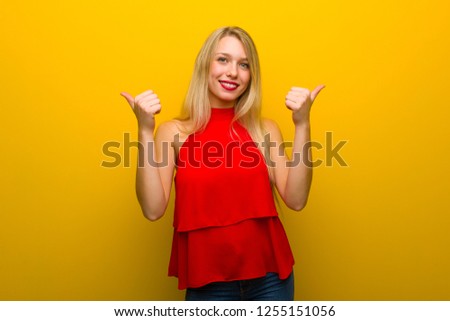 Young girl with red dress over yellow wall giving a thumbs up gesture with both hands and smiling