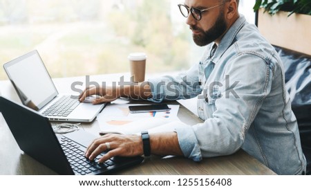 Side view. Hipster bearded businessman sits in cafe, modern office, works on two laptops. Freelancer works remotely. Student is preparing for exams. Startup. Online marketing, education for adult. Royalty-Free Stock Photo #1255156408