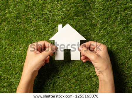 Conceptual picture of woman hands holding white house over green grass field top view and copy space in Property investment Real estate Saving and buying a home mortgage and loan banking concept.