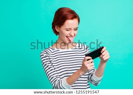 Close up portrait of cheerful ginger she her lady with telephone in hand trying to play new internet video game on telephone make faces wearing white striped sweater isolated on teal background