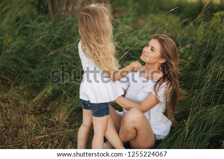 Attractive Mom and blonde hair daughter sits on road near big alley. They smile and look to natune