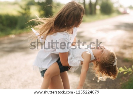little girl playing with mom in the park in summer day during the sunset