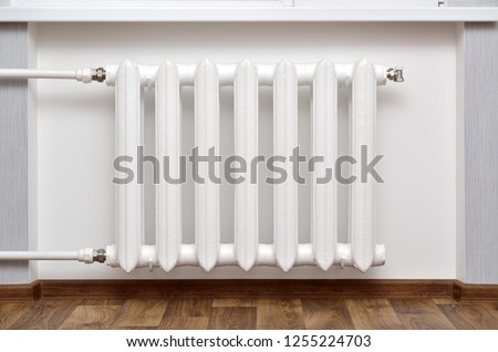 Pipes and a white heating radiator heat the room. Royalty-Free Stock Photo #1255224703