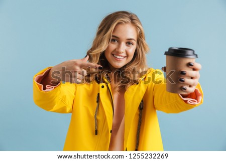 Portrait of cute woman 20s wearing yellow raincoat holding takeaway coffee isolated over blue background