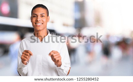 Young african american man with white shirt holding an empty white placard for insert a concept in the middle of the city