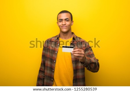 Young african american man on vibrant yellow background holding a credit card