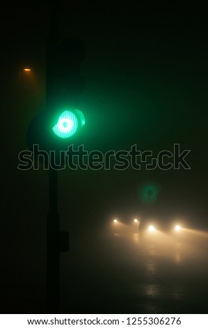 Green traffic lights and approaching vehicles in dense fog at night. Traffic, safety, traffic accident and visibility concepts.