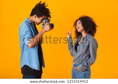 Cheerful young african couple standing isolated over orange background, making a video with camera
