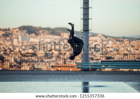 Brunette and strong guy jumping from trampoline at sunset in pool in Barcelona city
