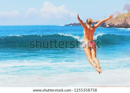 Happy family vacation. Girl in bikini jump high with spreading hand into mid air above water pool and breaking sea surf. Travel adventure lifestyle on summer beach holiday with kids on tropical island