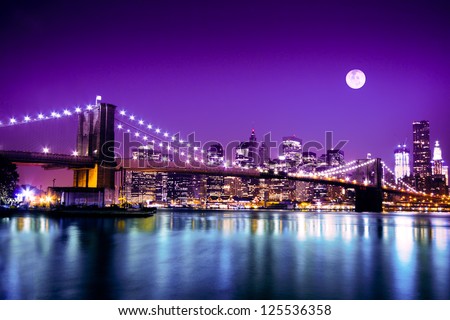 The Brooklyn Bridge lit up at night and the downtown Manhattan skyline under a full moon