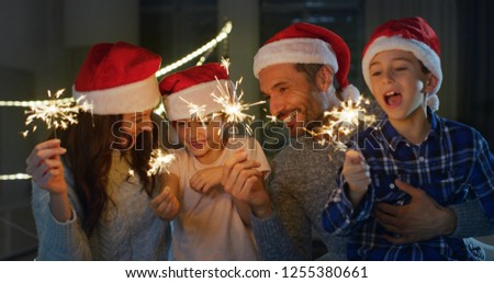Portrait of happy family celebrating Christmas singing with santa hats in the evening. Concept of holidays, Christmas, happy family, joy.