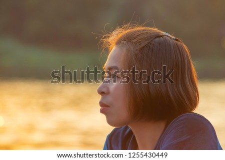 Portrait of Asian woman sitting by the river and the reflected light gold in water.