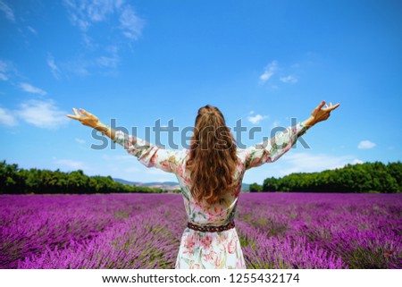 Seen from behind young woman in long dress at lavender field in Provence, France rejoicing. Perfect image of provencal summer for social media profile. Vibrant lavender meadow in beginning of August.