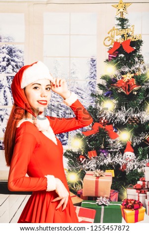 Young red head girl in a Santa Claus mini dress on a christmas background with gifts