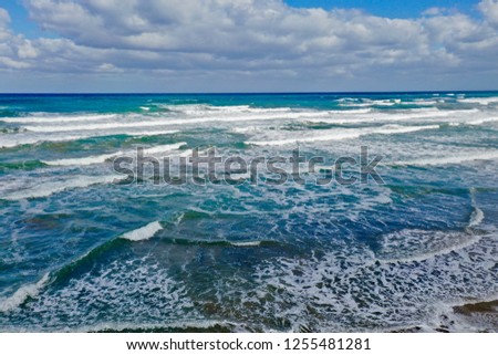 Waves rolling to the beach by Georgioupoli, Crete, Greece showing colors from turquoise to dark blue, sky clouds and sand for backgrounds and wallpaper