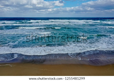 Waves rolling to the beach by Georgioupoli, Crete, Greece showing colors from turquoise to dark blue, sky clouds and sand for backgrounds and wallpaper