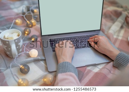 Enjoying Christmas at home. Young woman working on laptop and drinking coffee while sitting on a floor at home. Top view mockup image of girl using and typing on laptop with blank white screen.