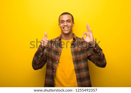 Young african american man on vibrant yellow background showing ok sign with and giving a thumb up gesture