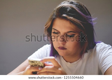 beautiful photo of Caucasian young female with brown hair and purple strands of hair,sitting in cove,drinking coffee and looking at her phone