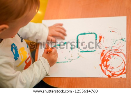 child draws on a sheet of paper stencils of geometric shapes, learning to paint in gouache, children's drawing