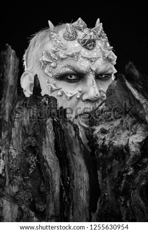 Tree spirit and fantasy concept. Monster with sharp thorns and warts. Druid behind old bark on black background. Man with dragon skin and bearded face. Goblin with horns on head.