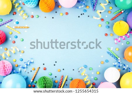 Birthday party background on blue. Top view. Frame made of colorful serpentine, balloons, candles, candies and confetti.
