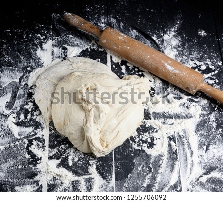 white wheat flour dough and wooden rolling pin on a black table
