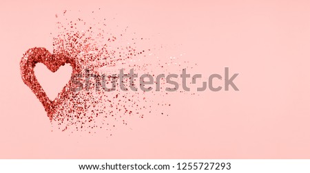 Glitter heart dissolving into pieces on pink background.  Valentines day, broken heart and love emergence concept. Horizontal wide screen banner format. Living coral theme - color of the year 2019