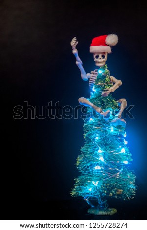 A skeleton hanging onto the top of a lit up Christmas Tree.