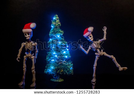 Skeletons dancing around a Christmas Tree with lights.