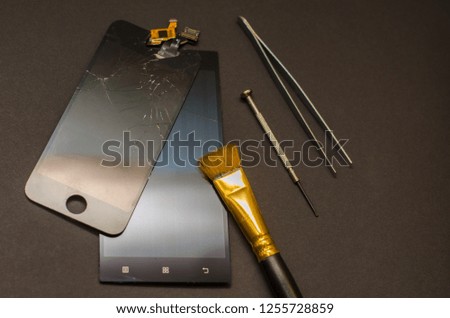 repair of mobile phones and smartphones. The broken screen lies on the table next to the tools. Black background.