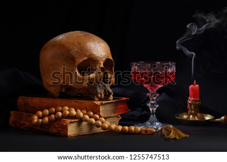 Still life with a skull on old books, with a glass of red wine, rosaries and a extinguished candle on a dark background