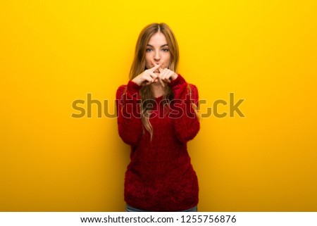 Young girl on vibrant yellow background showing a sign of silence gesture