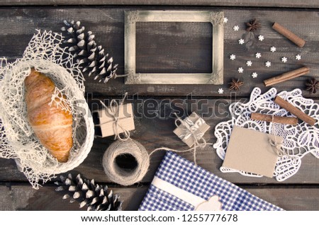 Autumn and winter background of rustic photo empty frame,gift box,ribbon,blue cloth,pine cones,lace,cinnamon sticks,snowflakes,anise spice and fresh croissant in basket.Above flat lay 