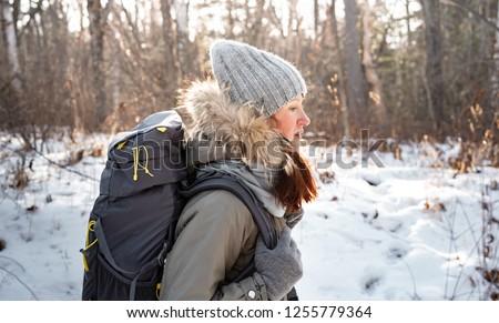 Hiking: A girl in a warm hat with red hair and a large backpack goes on foot in the winter forest.