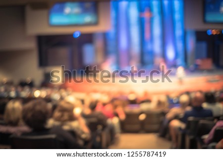 Vintage tone blurred abstract Christian people inside church listening to preacher speaking. Defocused back view audience on row of raised sitting chairs looking at stage with video projector screens