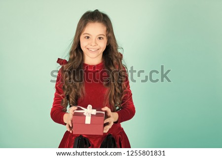 Happy child in red dress hold box on blue background. Girl with long brunette hair smile with present. Birthday, new year, christmas holidays. Gift giving, celebration. Boxing day concept, copy space