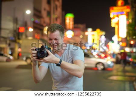 Young happy tourist man photographing with camera in the streets of Chinatown at night