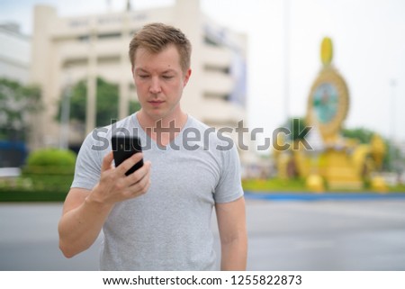 Young tourist man using phone against Ratchadamnoen street in Bangkok