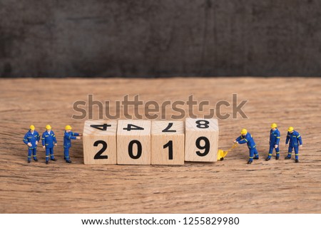 New year 2019 is coming concept, cute miniature people uniform worker staffs finish building cube wooden block as year number 2019 on wood table with dark blackboard background with copy space.