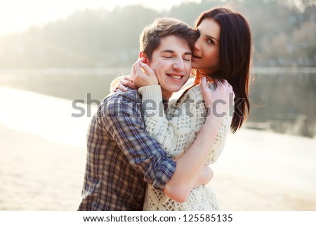 Young beautiful couple in love staying on the beach in evening sunshine. Happy smiling boy and girl