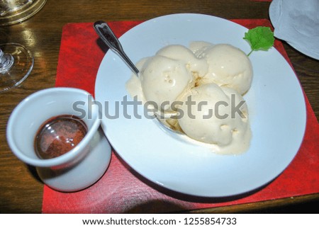 Bowl full of Ice cream and red placemat with bowl of chocolate sauce