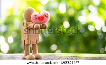 A man model made of wooden stand holding heart-shaped The background is a bokeh from a tree. Concept send heart on special day, valentine.