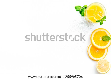 Orange juice with ice cubes. Juice in glass near cut orange and lemon, crushed ice, green mint on white background top view copy space
