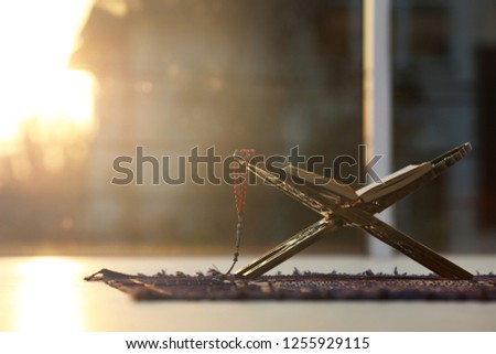 Rehal with open Quran and Muslim prayer beads on rug indoors. Space for text Royalty-Free Stock Photo #1255929115