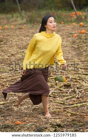 Adult woman dancer in a yellow blouse and brown dress, running in a pumpkin patch on a farm in Ellington, Connecticut.